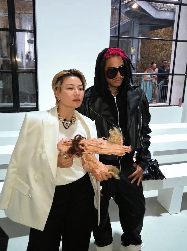 Une sculpture rose composée de poupées, tenue au premier plan lors d’un défilé au Palais de Tokyo à Paris.